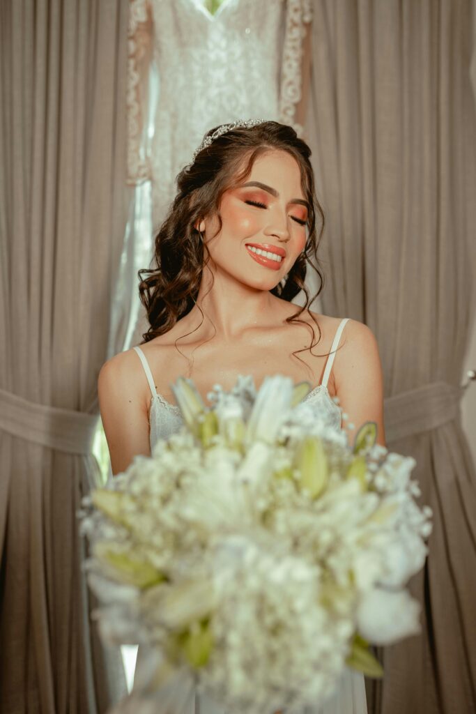 Stunning bride holding a white bouquet indoors on her wedding day, smiling with joy.