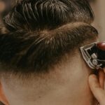 A tattooed barber uses electric clippers for a stylish haircut on a customer in a barber shop.